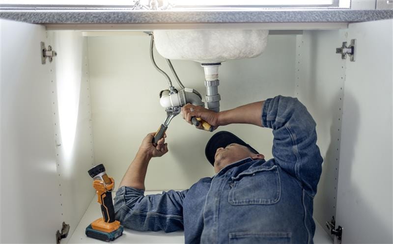 Plumber repairing pipes beneath a bathroom sink in Palm Harbor