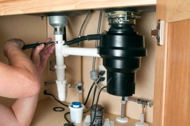 Plumber repairing a garbage disposal beneath a kitchen sink in Palm Harbor
